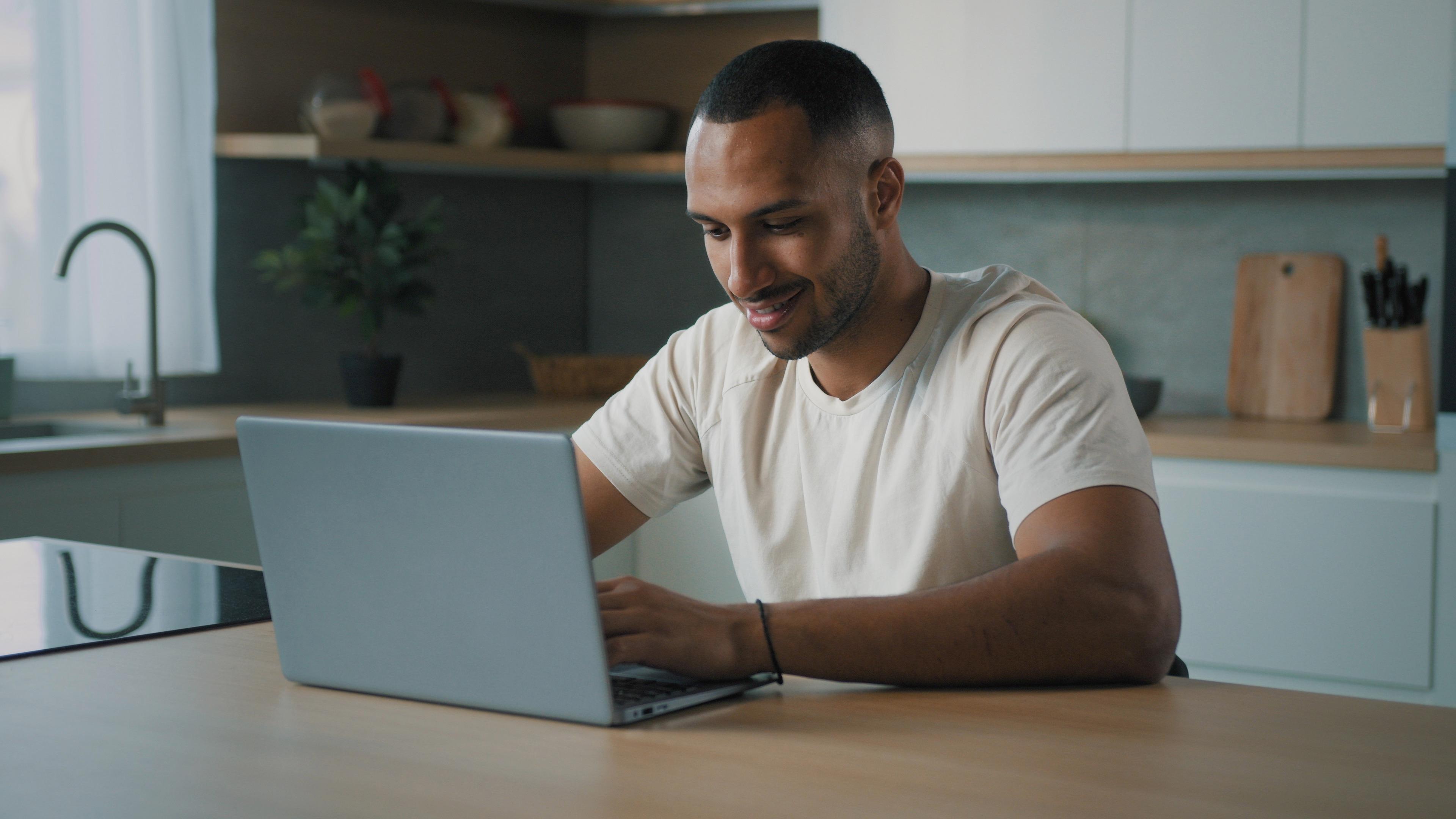 A man sitting at a kitchen table using a laptop.