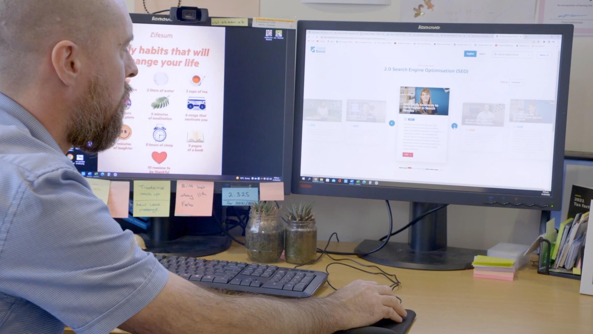 A man sitting at a desk with two monitors in front of him.