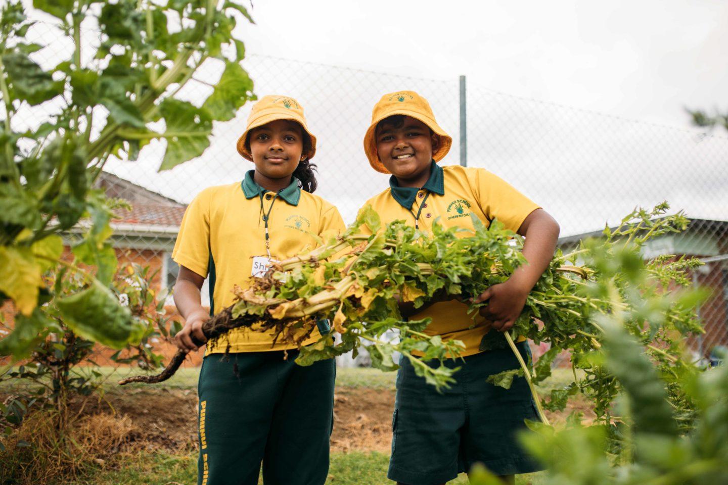 Two school students are holding a harvest from the school garden